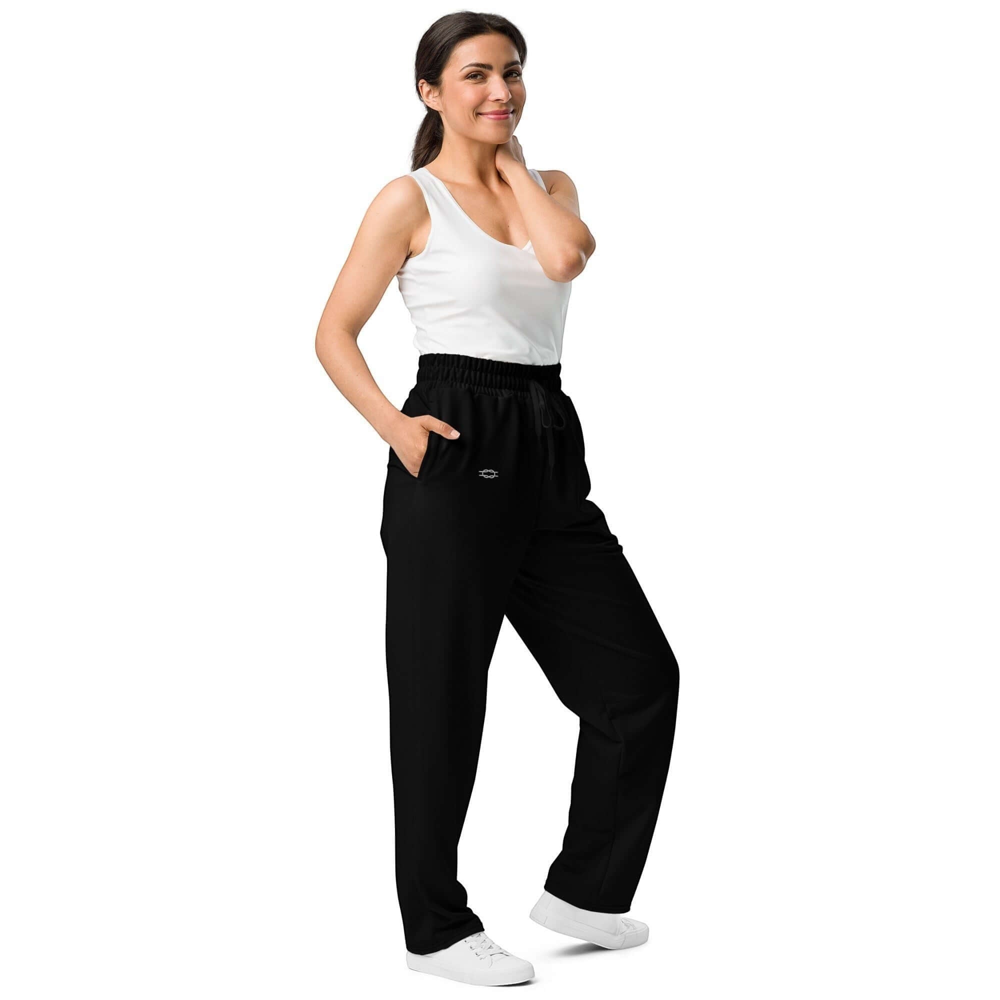 A woman wearing Urban Halo black wide-leg joggers with a white tank top and sneakers, standing against a white backdrop.